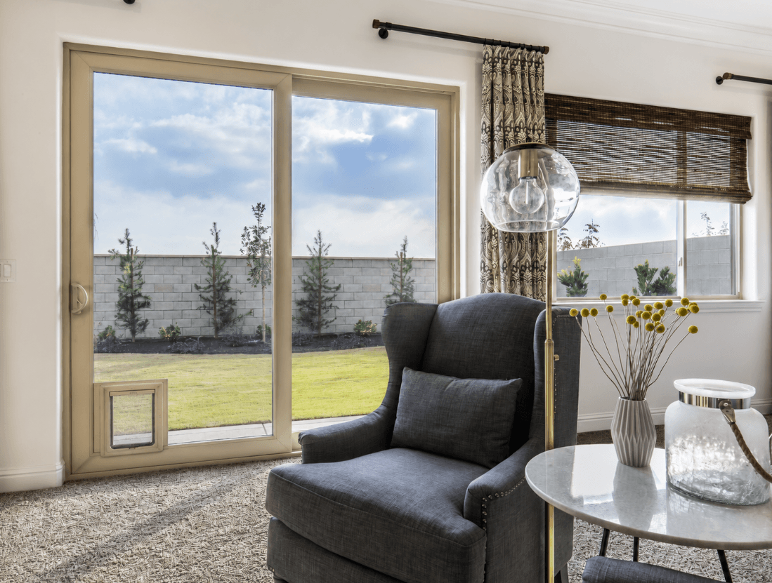 Living room with a tan-framed sliding patio door featuring an integrated pet door in the lower panel, opening to a backyard lawn