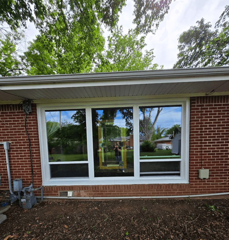 A fixed picture window flanked by two operable single-hung windows fills a brick living room with unobstructed natural light